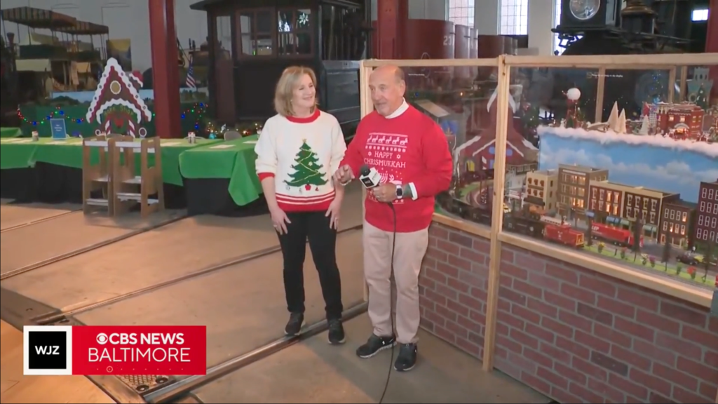 This is an image of a woman and man standing next to a holiday model train display.